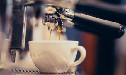 Disparo de una máquina de café espresso sirviendo café en una taza blanca en una cafetería.